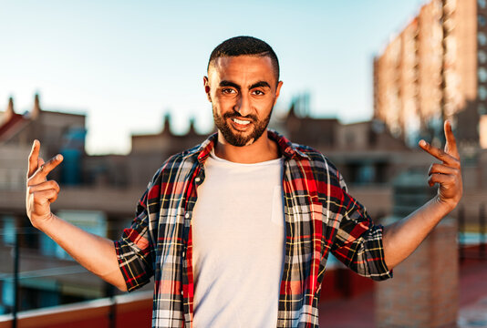Young man showing hip-hop gesture while standing on rooftop in city