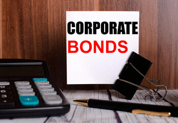 CORPORATE BONDS is written on a white card on a wooden background next to a calculator and pen.