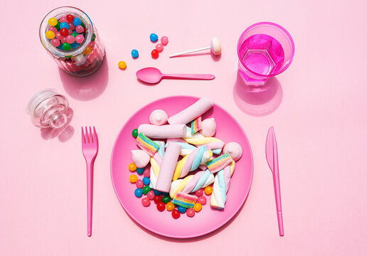 Studio shot of glass of water, jar of candies and plastic plate filled with various sweets