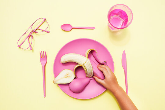 Hand of baby girl picking up pink-colored banana from plastic plate