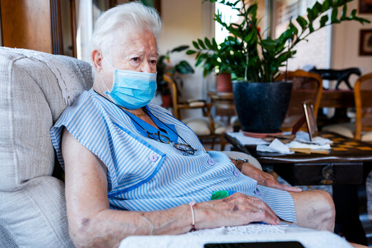 Female senior with protective mask sitting in armchair at home