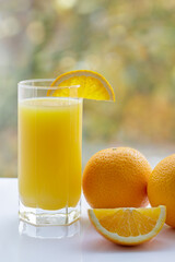Fototapeta premium Orange slice with two whole oranges and glass of juice on white table