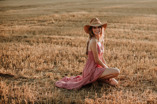 Smiling young woman kneeling in wheat field during sunset