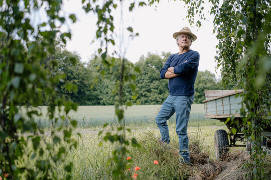 Thoughtful man wearing hat with arms crossed standing in yard