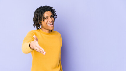 Young black man wearing rasta hairstyle stretching hand at camera in greeting gesture.