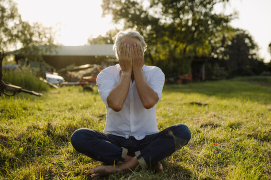 Man covering face while practicing yoga in yard