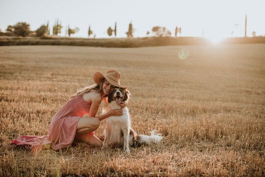 Woman embracing border collie dog in wheat field during sunset