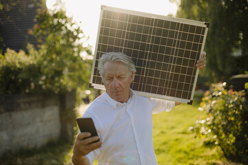 Man holding solar panel while using phone in yard