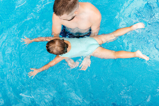 Little girl lerning to swim with her uncle in swimming pool