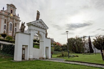 Naklejka premium The white baroque entrance gate in Fulnek, Czech Republic with a Kostel Nejsvetejsi Trojice (Holy Trinity Church) in background