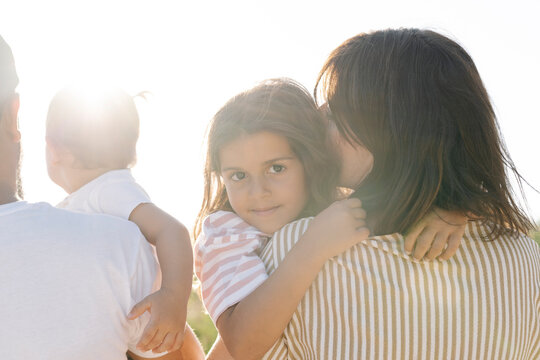 Cute girl embracing mother by father with sister at park during sunset