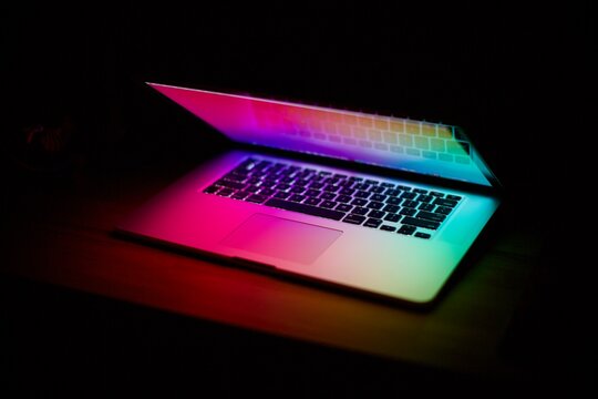 Close up and blurry view of laptop keyboard with colored lights in the dark background 