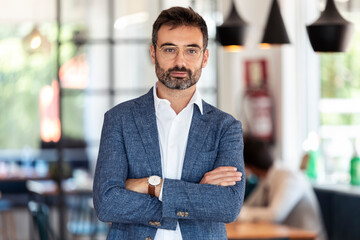 Confident businessman standing with arms crossed in restaurant