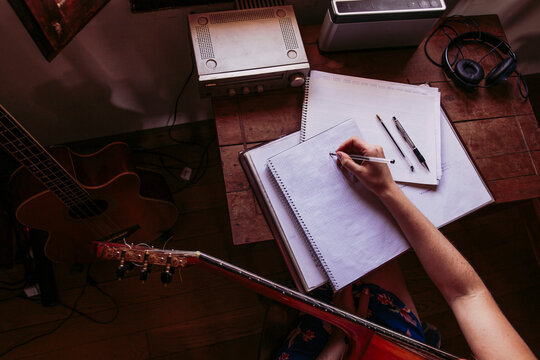 Young woman writing in book while practicing guitar at home