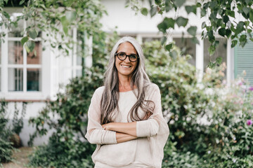 Portrait of smiling woman with long grey hair wearing spectacles standing in the garden