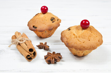two cupcakes with red cherries cinnamon and star anise on a white wooden table close up