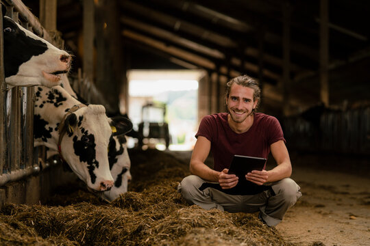 Portrait of a smiling young farmer with tablet at cow house on a farm