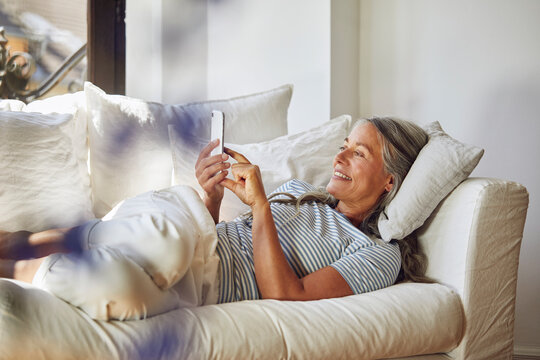 Smiling woman using phone on sofa in living room
