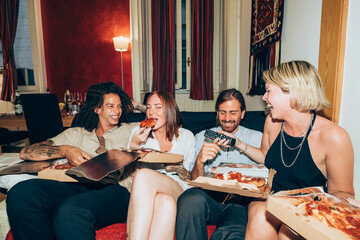 Happy friends eating pizza while sitting on sofa in living room