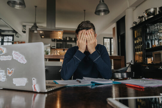 Overstressed young man studying from home, covering face with his hands