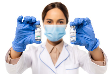 Selective focus of doctor in latex gloves holding jars with coronavirus vaccine lettering isolated on white