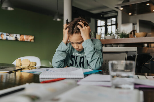 Schoolboy learning at home, head in hands, solving problem