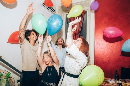 Happy carefree friends dancing with balloons during party at home