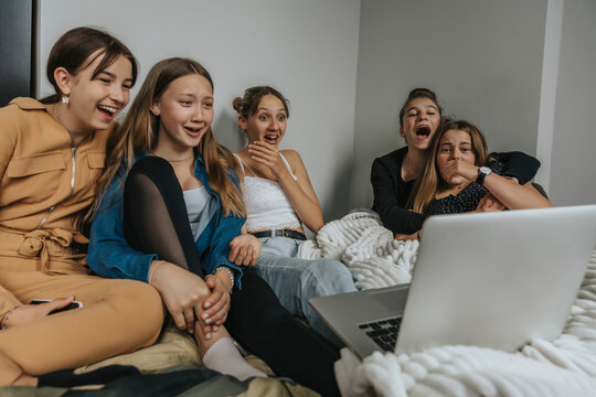Group of girlfriends sitting on bed, watching movie on laptop