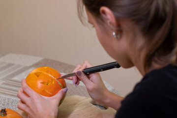 the process of making a Halloween pumpkin. cutting out the mouth by brunette girl. horror theme and Hallowe'en. 