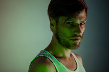 Handsome man standing against gray background and green lighting