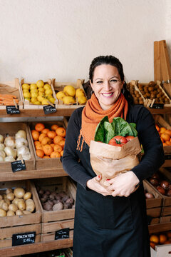Cheerful saleswoman holding bag of vegetables standing against boxes at store