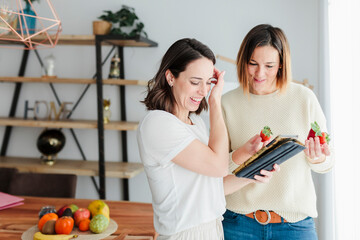 Friends learning about nutrition while holding strawberry and digital tablet at home
