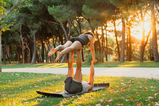 Male and female athletes practicing acroyoga in park during sunset