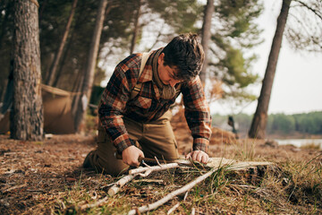 Bushcrafter cutting stick while kneeling in forest