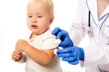 Selective focus of pediatrician in latex gloves holding cotton near hand of toddler isolated on white