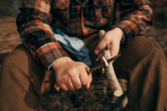 Bushcrafter cutting stick while sitting in forest