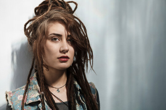 Young Rastafarian woman standing against gray wall