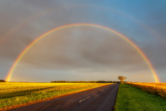 Double rainbow arching over empty countryside highway