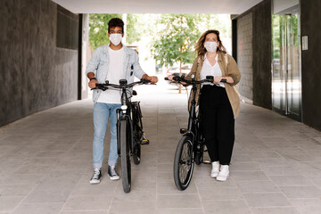 Couple in protective face masks standing with electric bicycles on footpath