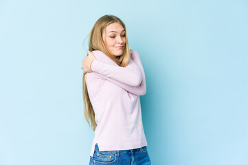 Young blonde woman isolated on blue background hugs, smiling carefree and happy.