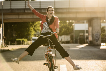 Cheerful woman enjoying cycling on street in city during sunny day