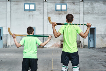 Father and son in uniform holding hockey sticks at sports court