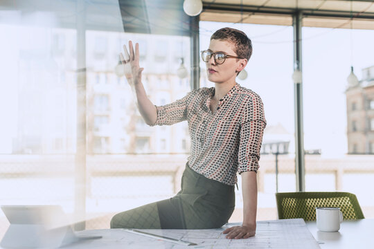 Businesswoman sitting on desk in office raising her hand