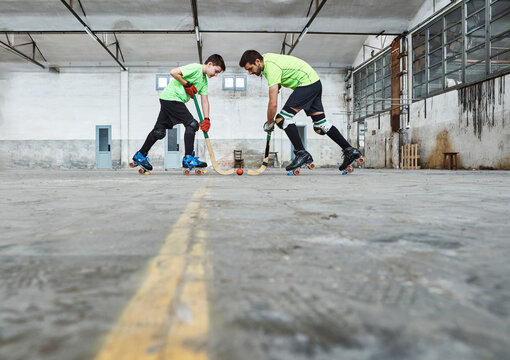 Surface level view of father and son in face off while playing roller hockey on court