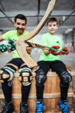 Close-up of hockey sticks held by father and son sitting on wooden box at court