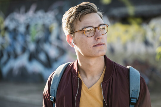 Handsome young man looking away while listening music through bluetooth earphones
