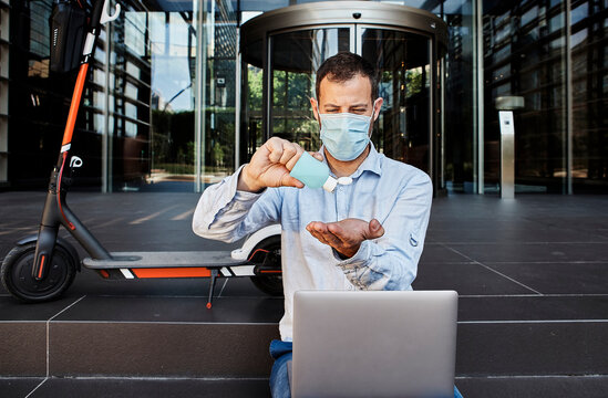 Entrepreneur with laptop sanitizing hands on staircase during coronavirus
