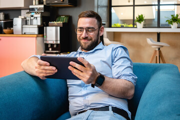 Smiling businessman using digital tablet for video call while sitting on armchair at office cafeteria