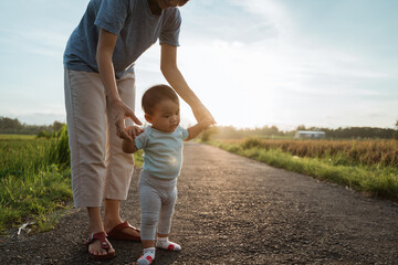 Fototapeta premium mother help her baby to walk her first step on country road