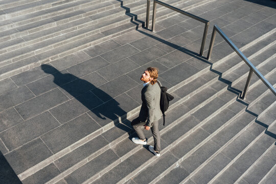 Male entrepreneur with bag moving up on staircase while looking away in downtown during sunny day